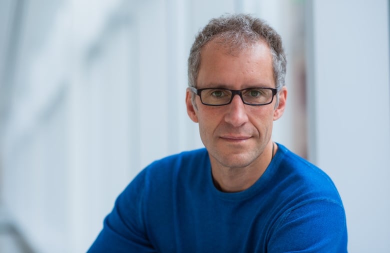 A man in a blue jacket and glasses looks at the camera.